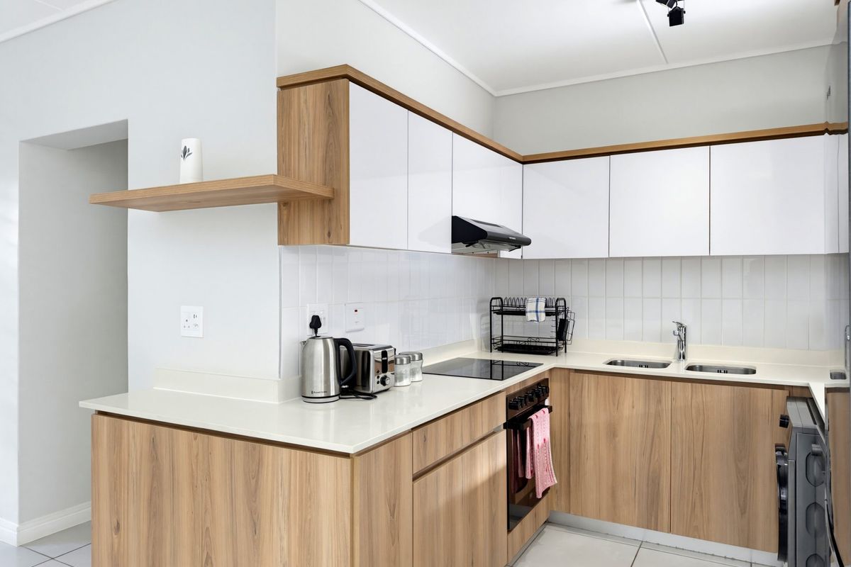 Modern kitchen featuring sleek wood-grain and white cabinetry, stone countertops, integrated appliances, and a clean tiled backsplash.
