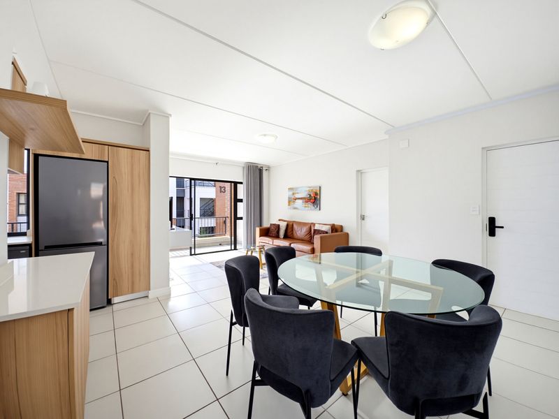 Modern open-plan living and dining area featuring tiled floors, neutral finishes, and direct access to a private balcony through sliding glass doors.