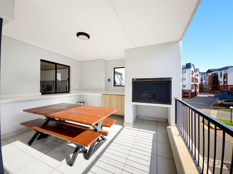 Covered balcony featuring a built-in braai, tiled flooring, and a metal balustrade, offering a functional outdoor entertainment space.