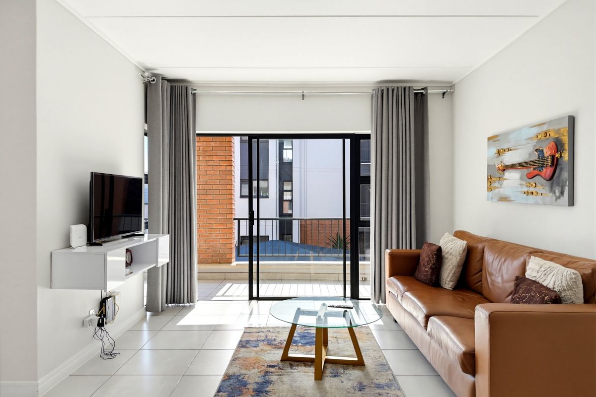 A bright living room featuring tiled flooring and a large sliding glass door that opens onto a private balcony.