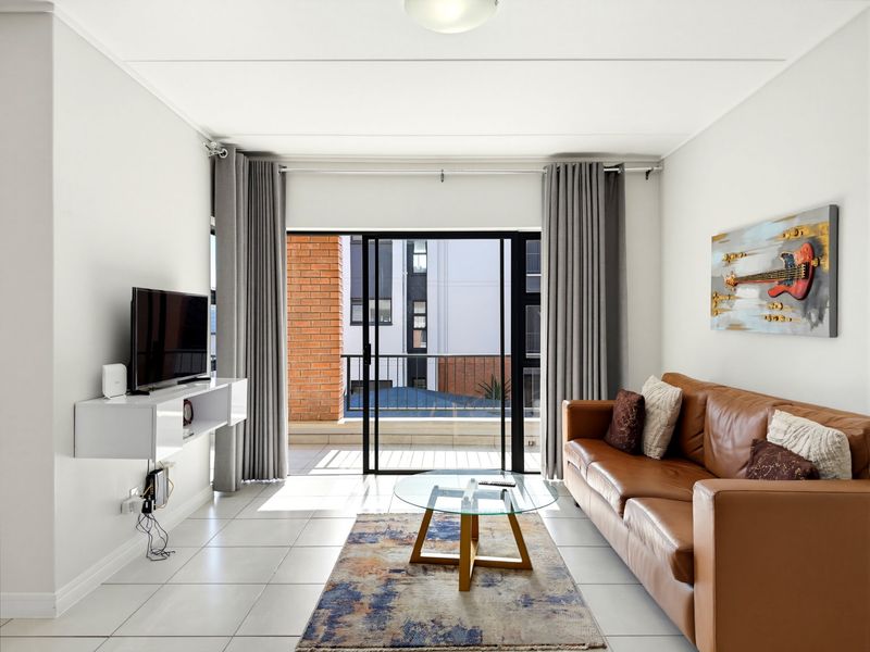 A bright living room featuring tiled flooring and a large sliding glass door that opens onto a private balcony.