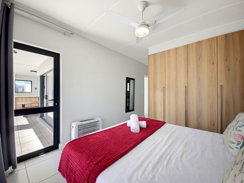 A bright bedroom featuring built-in wooden cupboards, a ceiling fan, tiled floors, and direct access to an outdoor patio through a sliding glass door.