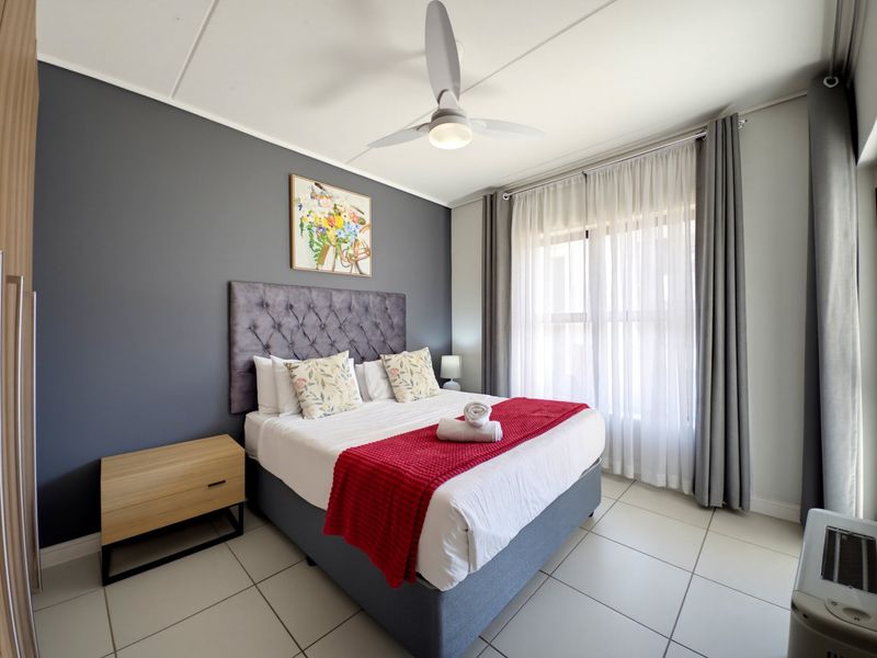 A well-maintained bedroom featuring tiled flooring, a ceiling fan, and a built-in wardrobe, offering a clean and comfortable living space.