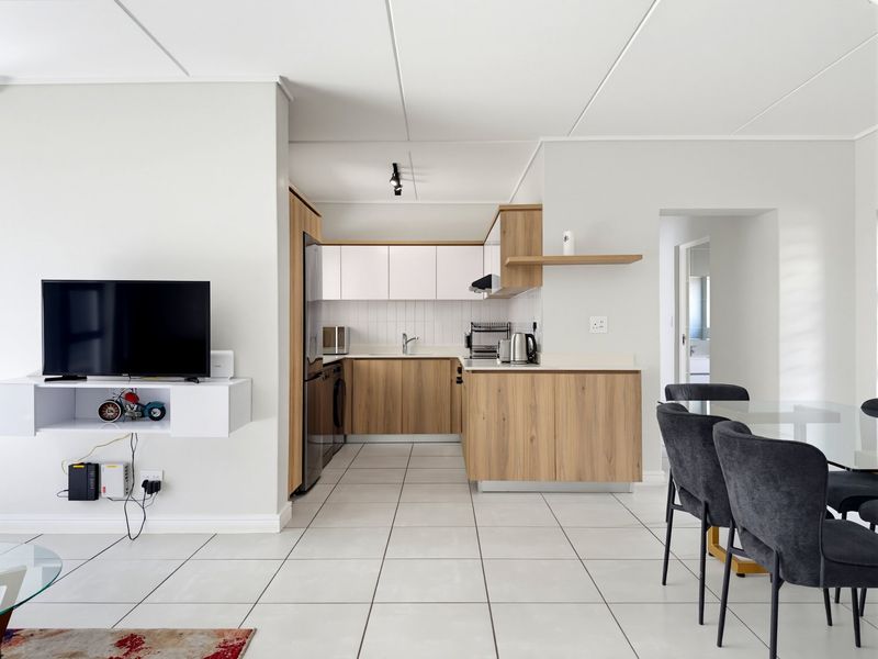 Modern open-plan living area featuring a contemporary kitchen with wood-finish cabinetry, white upper cabinets, and tiled flooring throughout.