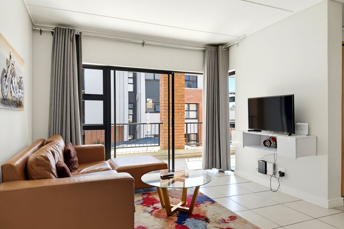 A bright living room featuring tiled flooring, a floating media console, and large sliding glass doors that open onto a balcony.