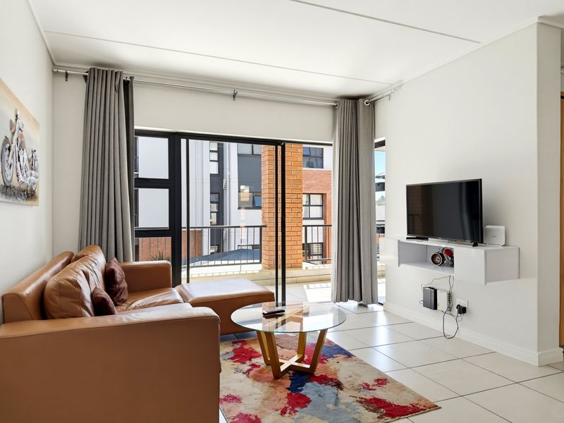 A bright living room featuring tiled flooring, a floating media console, and large sliding glass doors that open onto a balcony.
