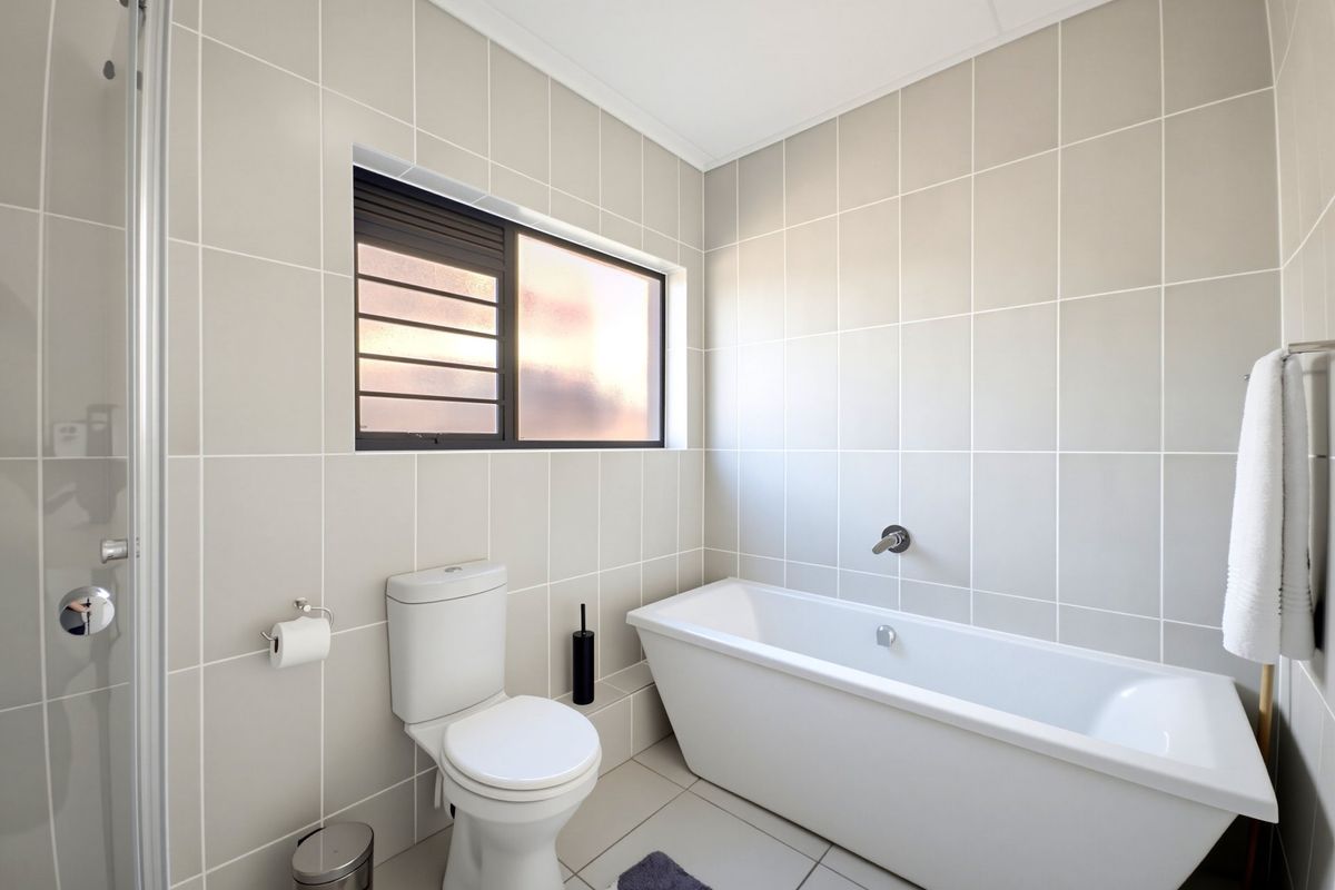 Modern bathroom featuring a freestanding bathtub, separate shower enclosure, and neutral floor-to-ceiling wall tiles with a frosted glass window for natural light.