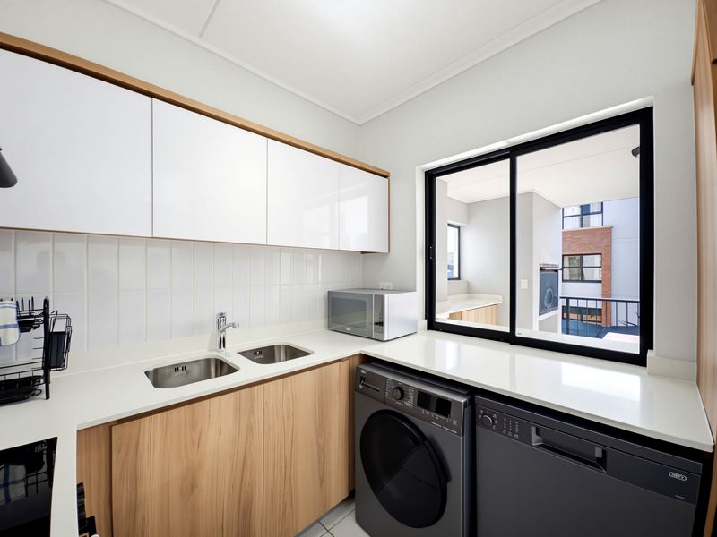 Modern scullery featuring sleek wood-finish cabinetry, white stone countertops, a double stainless steel sink, and a subway tile backsplash with integrated appliance space.