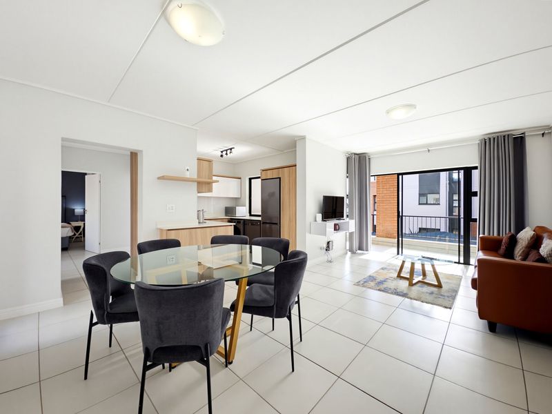 Bright open-plan living and dining area featuring tiled floors, modern kitchen cabinetry, and large sliding doors leading to a private balcony.