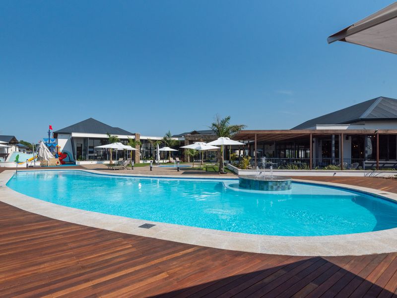 A well-maintained outdoor pool area featuring a large swimming pool with a built-in water feature, surrounded by timber decking and landscaped grounds.