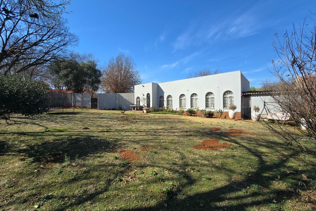 A rear view of the property featuring a large garden area and a single-story building with distinctive arched windows.