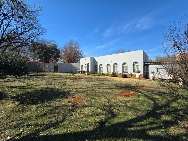 A rear view of the property featuring a large garden area and a single-story building with distinctive arched windows.