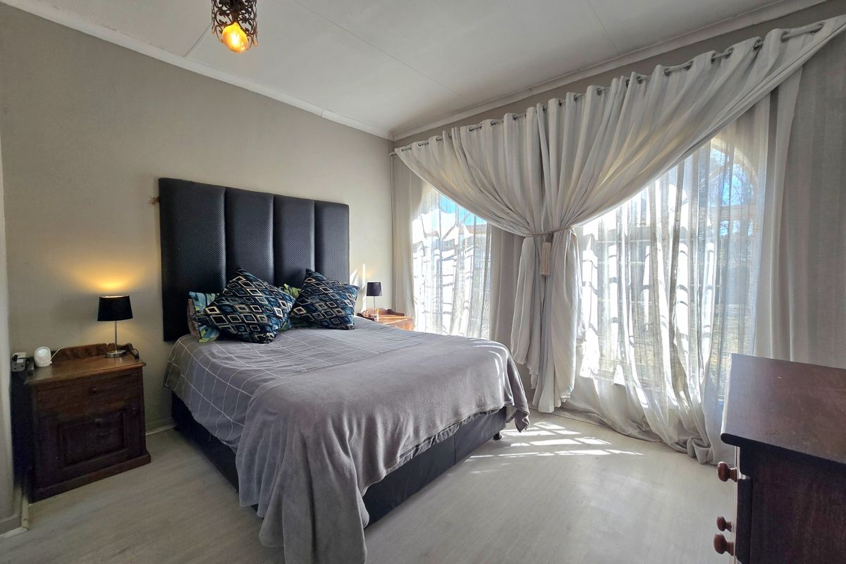 A well-lit bedroom featuring light-toned laminate flooring, neutral wall finishes, and a large window dressed with floor-to-ceiling curtains.