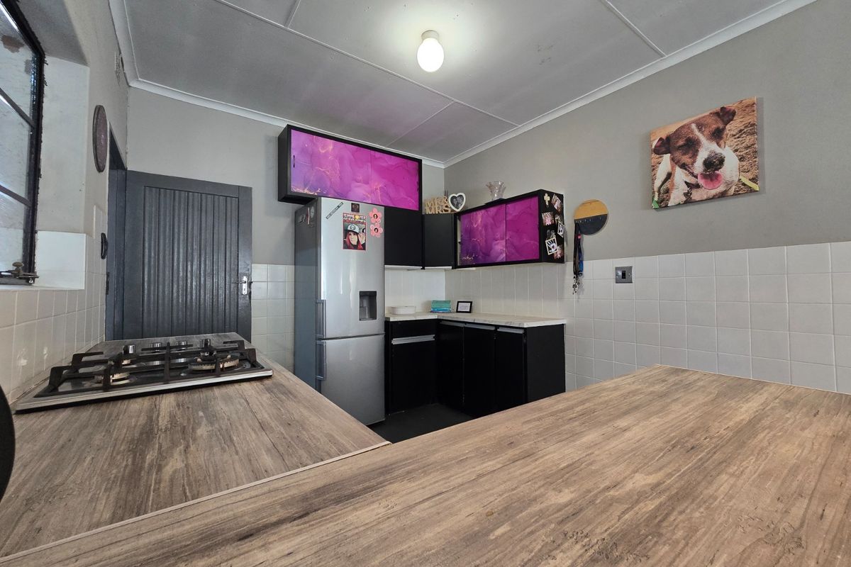 A functional kitchen featuring a gas hob, laminate countertops, tiled splashbacks, and dark cabinetry with decorative purple accents.