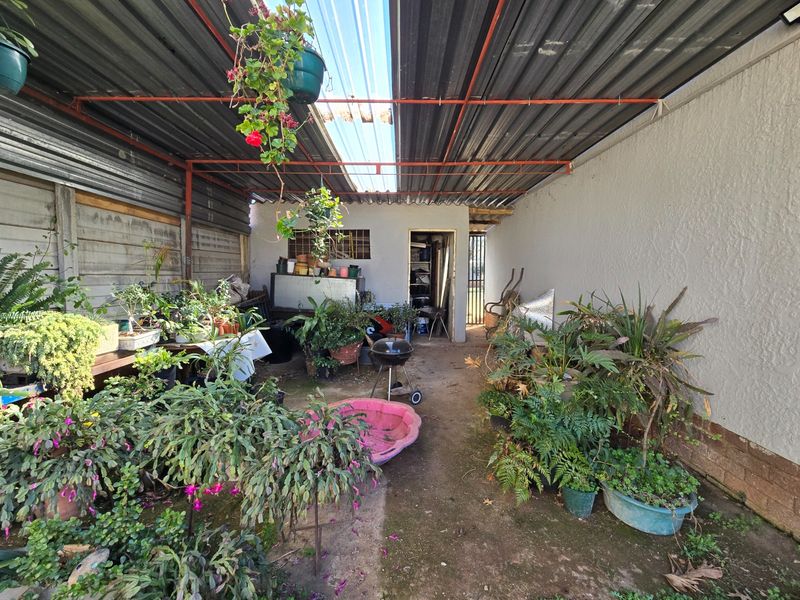A covered outdoor patio area featuring a corrugated metal roof with a translucent section, concrete flooring, and precast concrete boundary walls.