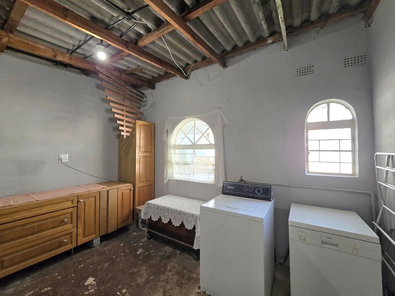 A functional laundry area featuring arched windows, exposed timber roof trusses, and built-in wooden cabinetry with existing plumbing connections.