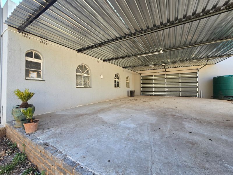 A spacious covered garage area featuring a corrugated metal roof, concrete flooring, and arched windows, providing ample secure parking space.