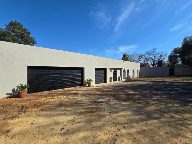 Front elevation of a property featuring a double and single garage, arched windows, and a clean stucco facade with an expansive unpaved driveway area.