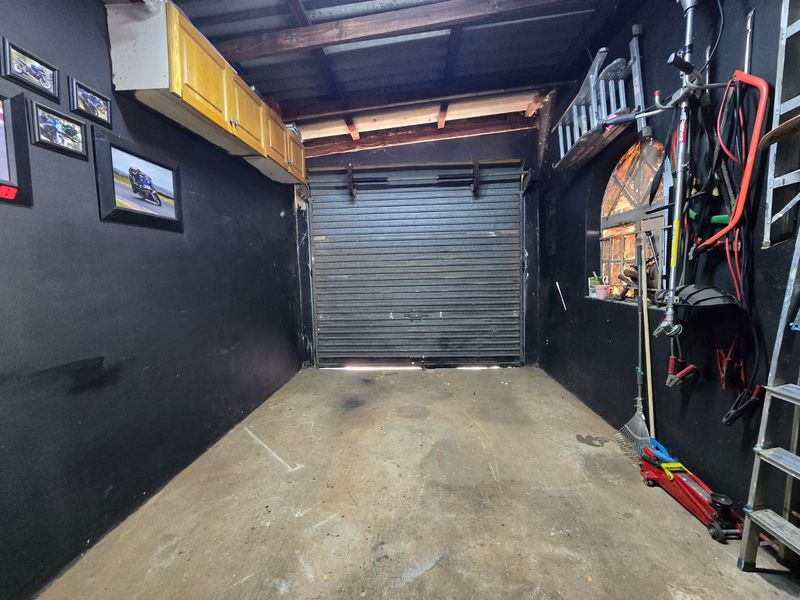 A functional garage space featuring a roller shutter door, exposed timber rafters, and an arched window, providing secure storage or workspace potential.