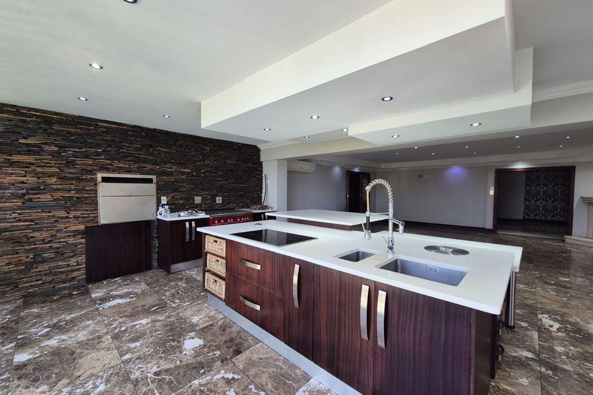 Modern kitchen featuring a large island with stone countertops, integrated sink, induction cooktop, and a striking stacked stone feature wall with built-in braai.