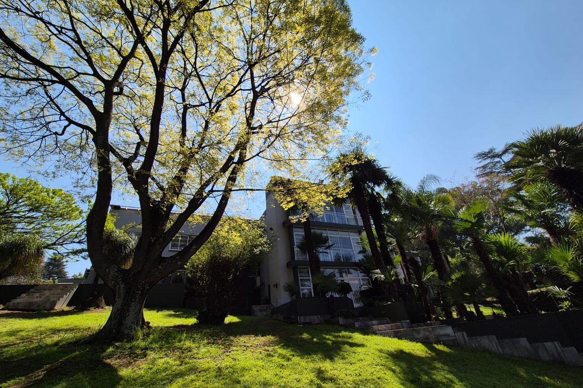 A view of the rear facade of the multi-story house, featuring large windows and a well-maintained garden with mature trees.
