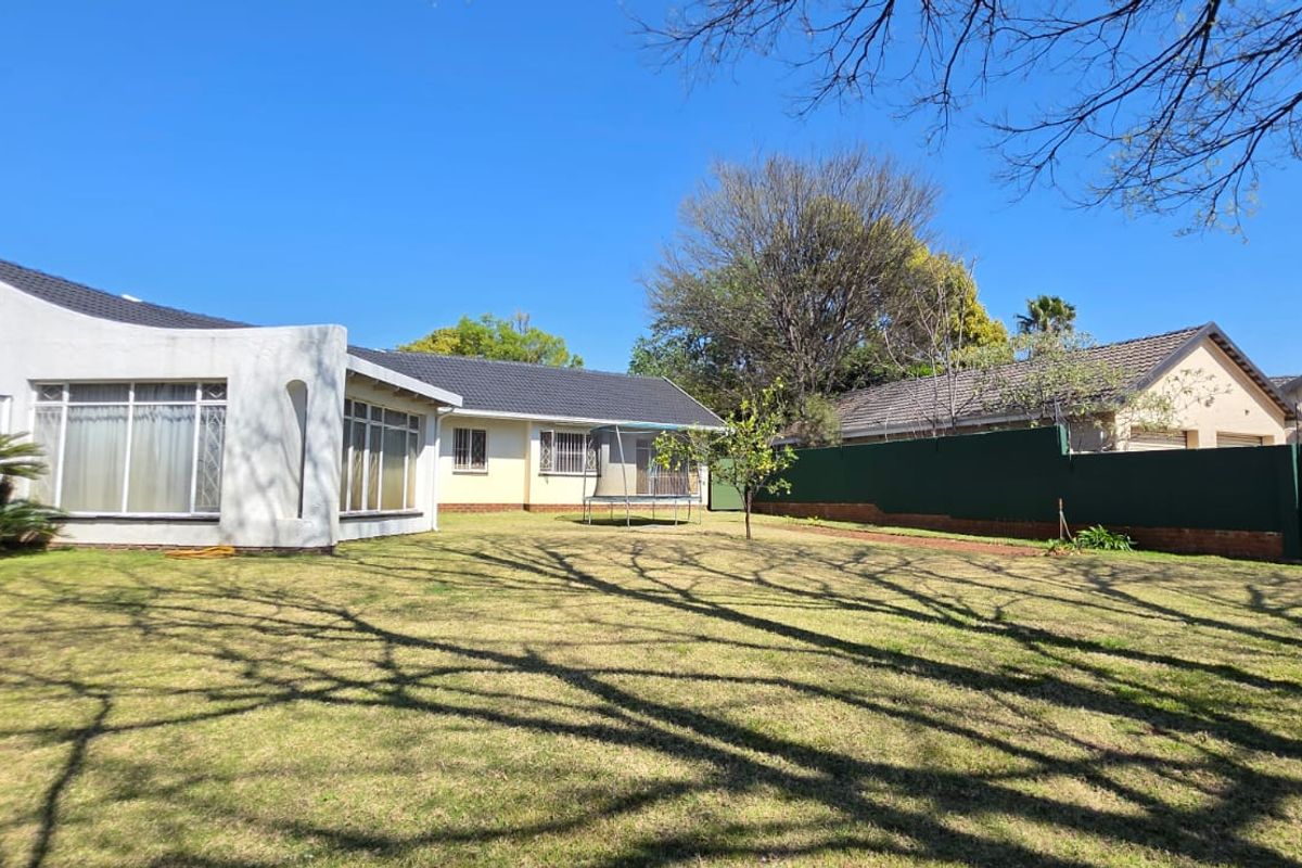 A view of the rear garden and the back elevation of the house, featuring a lawn and perimeter fencing.