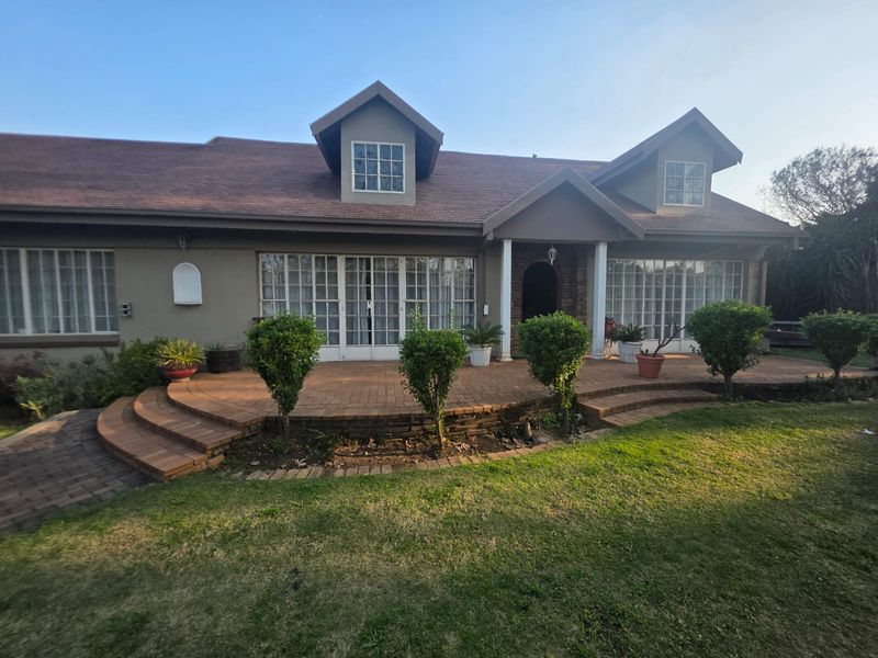 Rear view of the house featuring a spacious brick-paved patio, multiple sets of French doors, and charming dormer windows overlooking the garden.