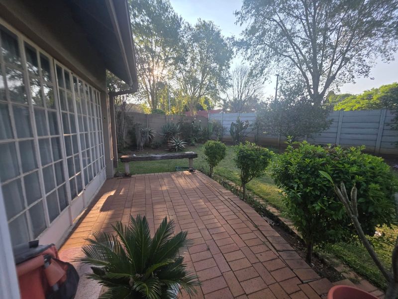 A paved outdoor patio area adjacent to the house, featuring a garden view and access through large french doors.