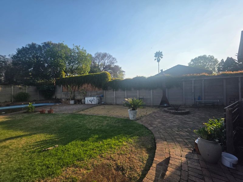 Spacious rear garden featuring a swimming pool, brick-paved patio area, fire pit, and perimeter walling with established greenery.
