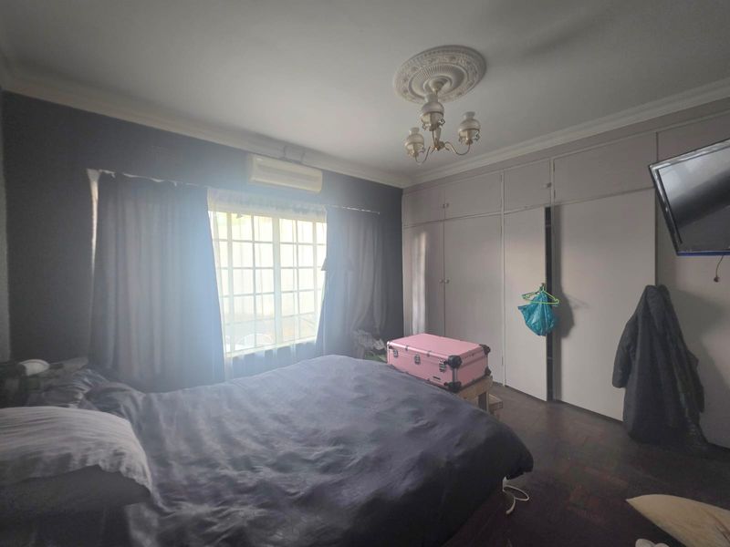 A bedroom featuring parquet flooring, built-in cupboards, a decorative ceiling rose with a chandelier, and a wall-mounted air conditioning unit.