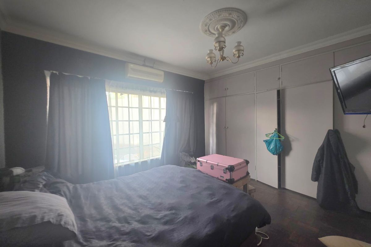 A bedroom featuring parquet flooring, built-in cupboards, a decorative ceiling rose with a chandelier, and a wall-mounted air conditioning unit.