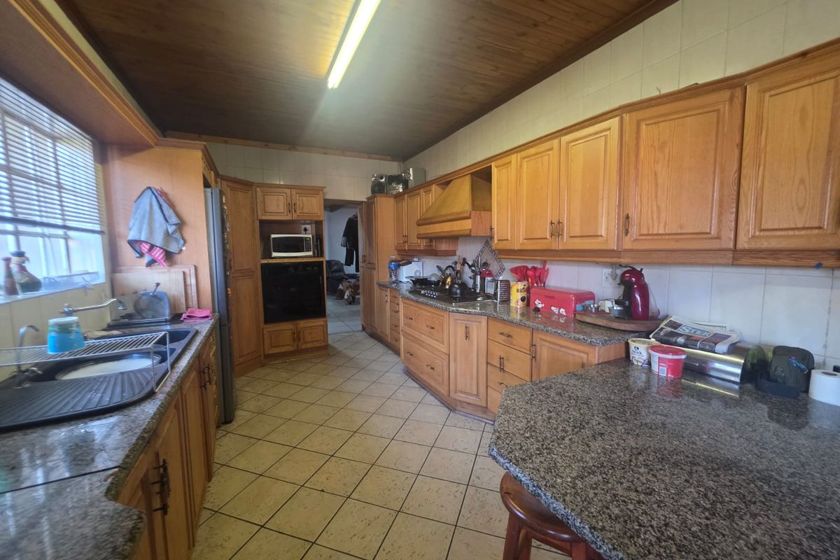A functional kitchen featuring granite countertops, extensive wooden cabinetry, built-in appliances, and tiled flooring with a timber-paneled ceiling.