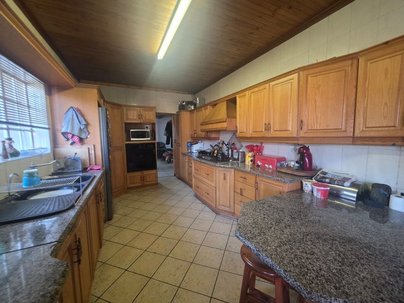 A functional kitchen featuring granite countertops, extensive wooden cabinetry, built-in appliances, and tiled flooring with a timber-paneled ceiling.