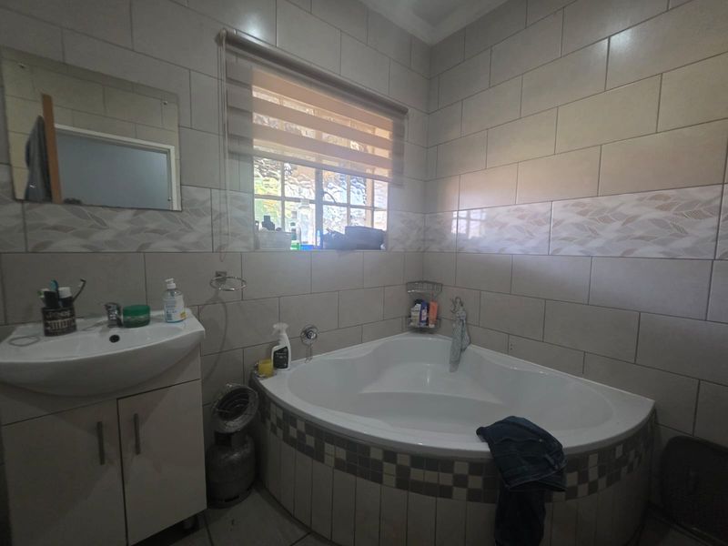 A functional bathroom featuring a corner bathtub, vanity cabinet with basin, and neutral wall tiling.