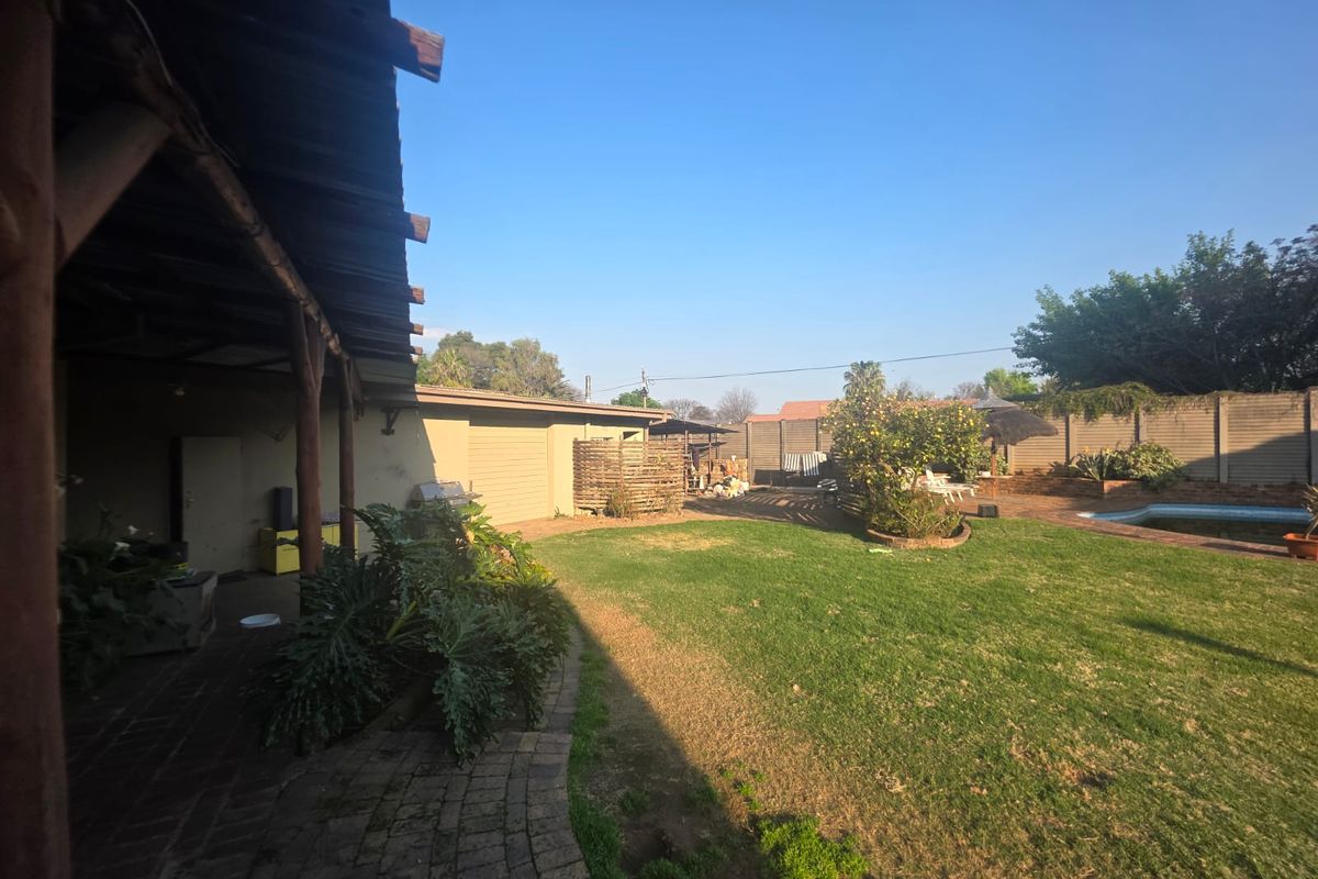 Spacious rear garden featuring a covered patio, swimming pool, and established lawn, enclosed by perimeter walling.