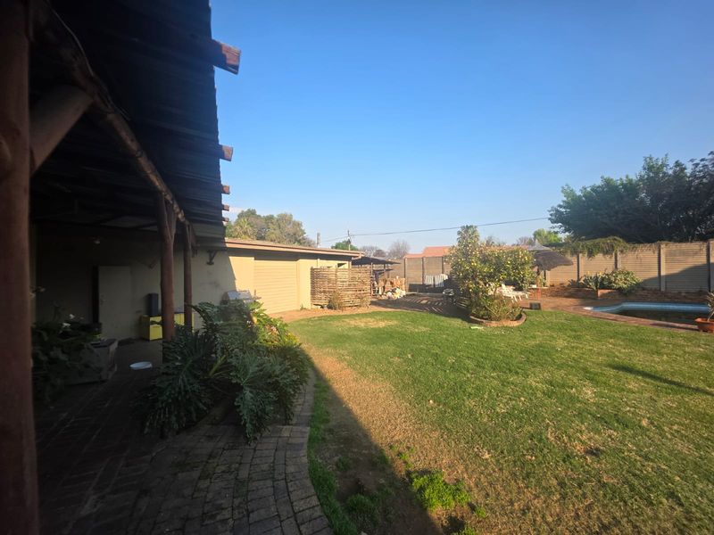 Spacious rear garden featuring a covered patio, swimming pool, and established lawn, enclosed by perimeter walling.