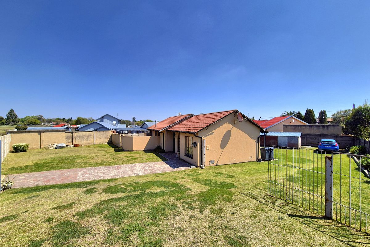 Rear view of the property featuring a tiled roof, paved driveway, and a spacious garden enclosed by perimeter walls.