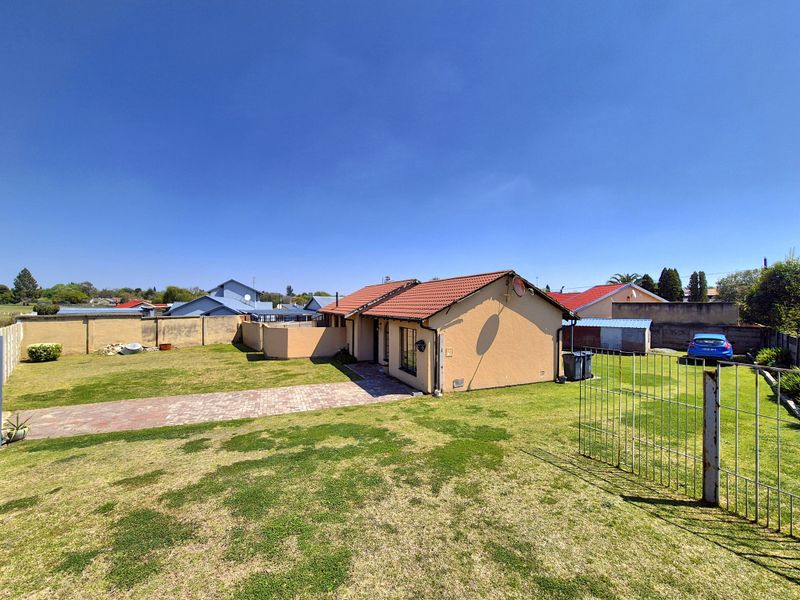 Rear view of the property featuring a tiled roof, paved driveway, and a spacious garden enclosed by perimeter walls.