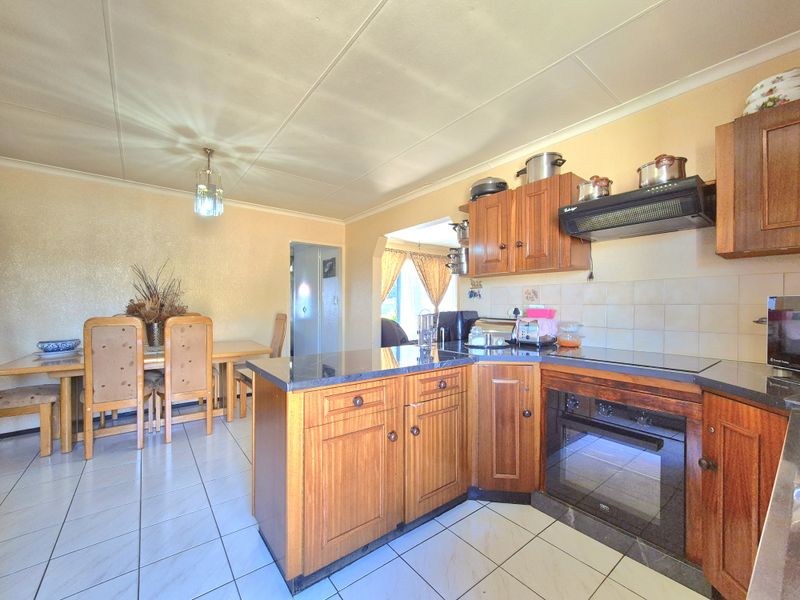 Open-plan kitchen and dining area featuring wooden cabinetry, built-in oven, electric hob, and tiled flooring throughout.