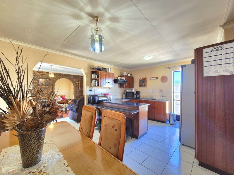Open-plan kitchen and dining area featuring tiled flooring, wooden cabinetry, and a distinctive brick archway leading to the adjacent living space.