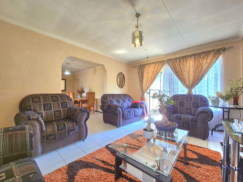 A living room featuring tiled flooring and an open-plan archway leading to the dining area, providing a functional and connected living space.