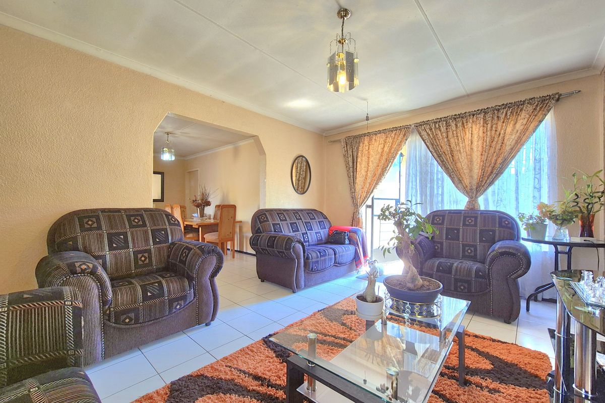 A living room featuring tiled flooring and an open-plan archway leading to the dining area, providing a functional and connected living space.