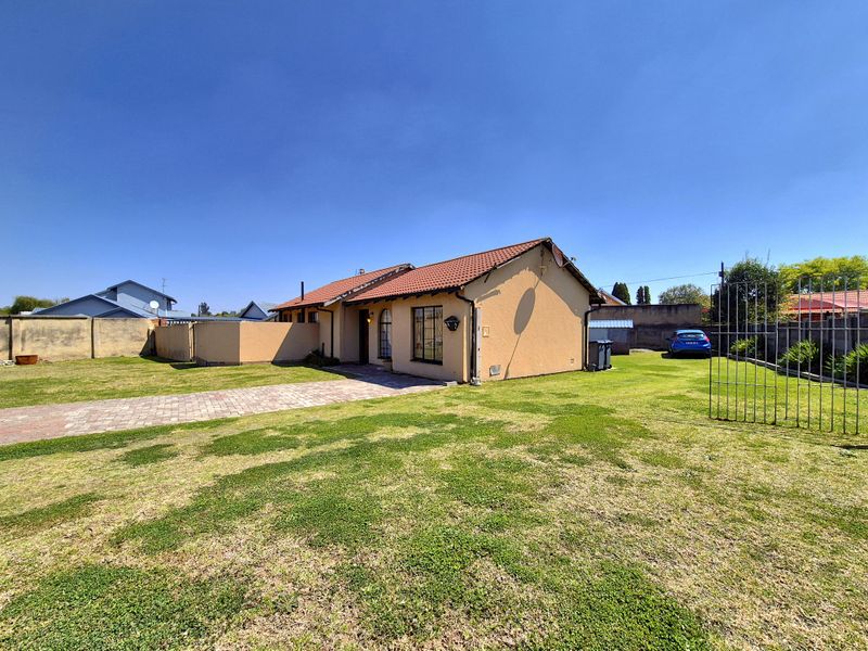 A detached single-story house featuring a terracotta tiled roof, paved driveway, and a large surrounding garden with perimeter boundary walls.
