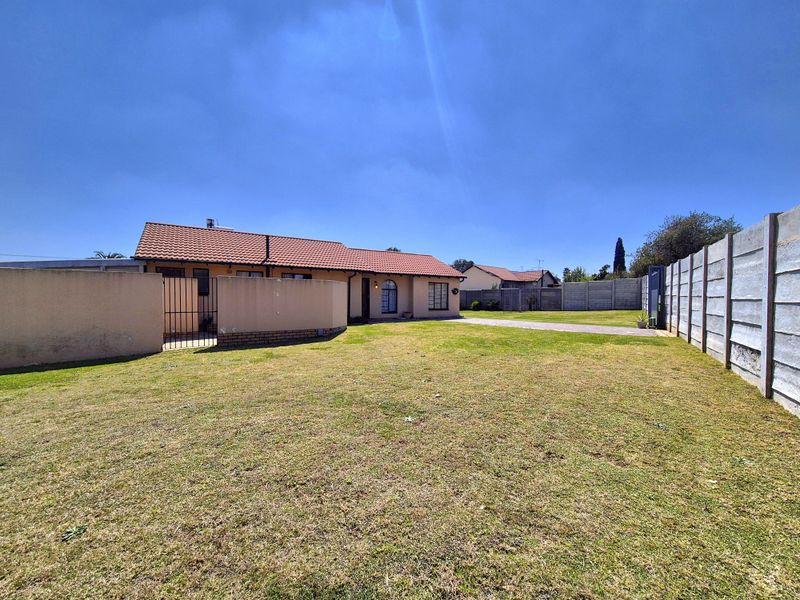A view of the rear exterior of the house featuring a tiled roof, expansive lawn, and secure precast concrete boundary walling.