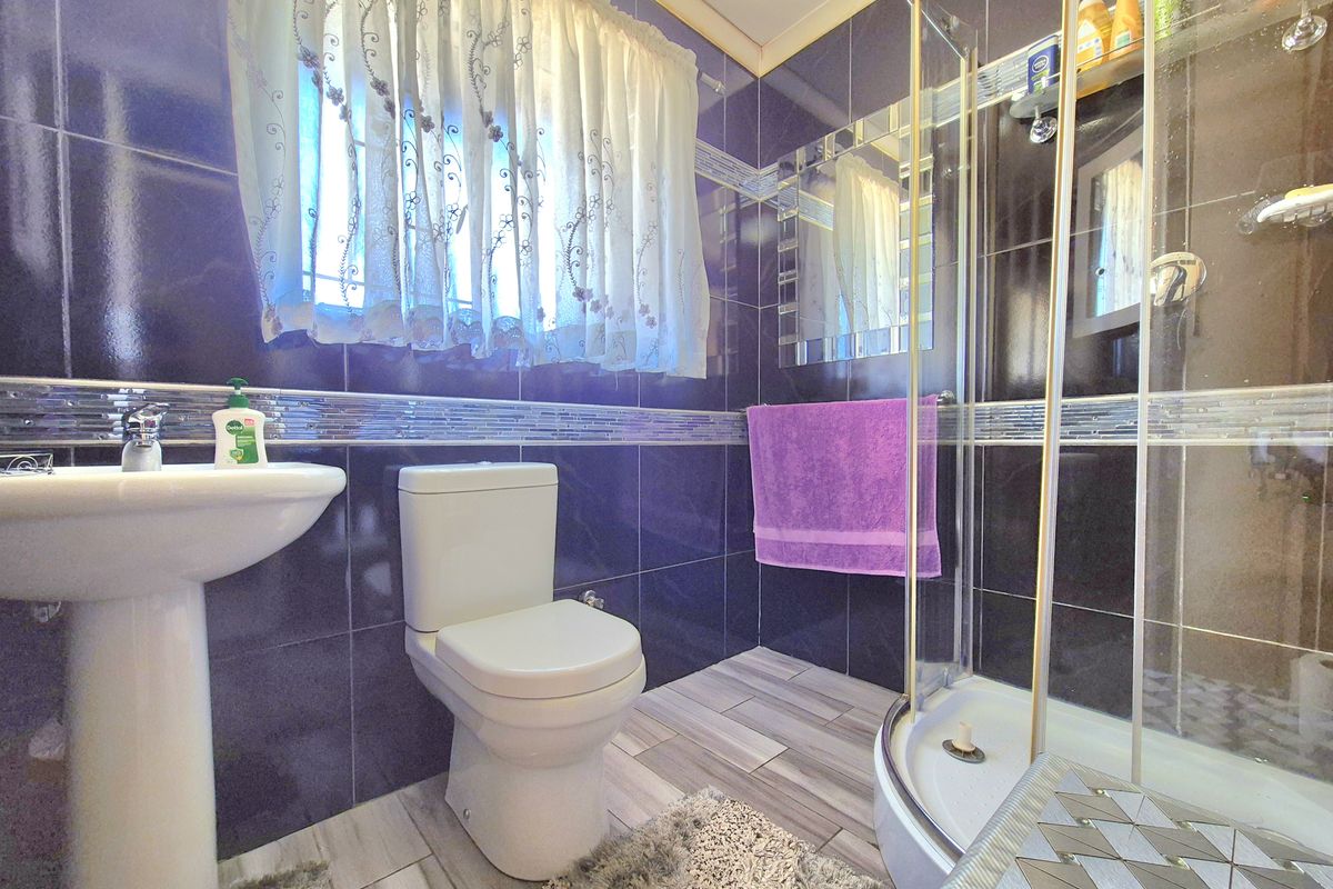 A compact bathroom featuring dark wall tiles, a pedestal basin, a toilet, and a corner shower enclosure with glass doors.