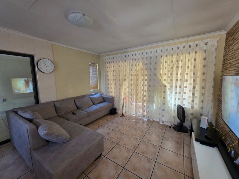A living room featuring tiled flooring, a sliding glass door with curtains, and neutral wall finishes, offering a functional space for relaxation.