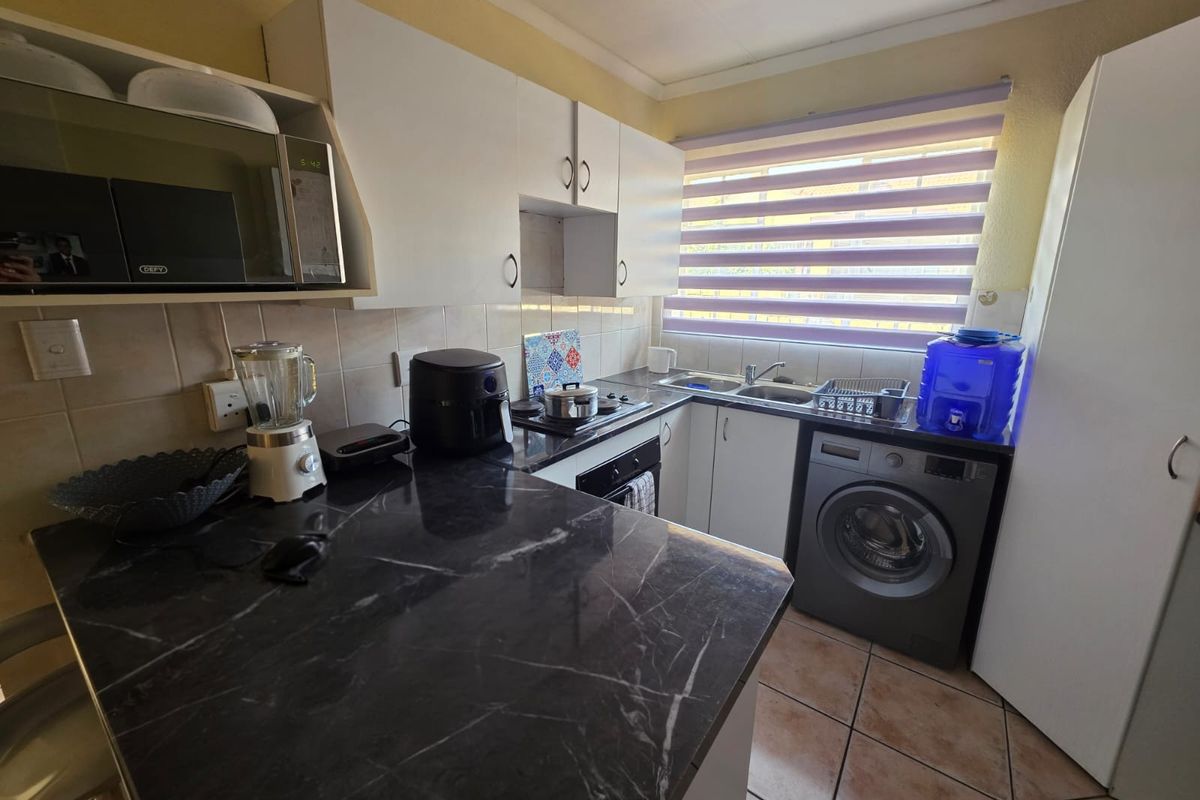 Compact kitchen featuring dark marble-effect countertops, white cabinetry, built-in oven, hob, and tiled flooring with space for a washing machine.