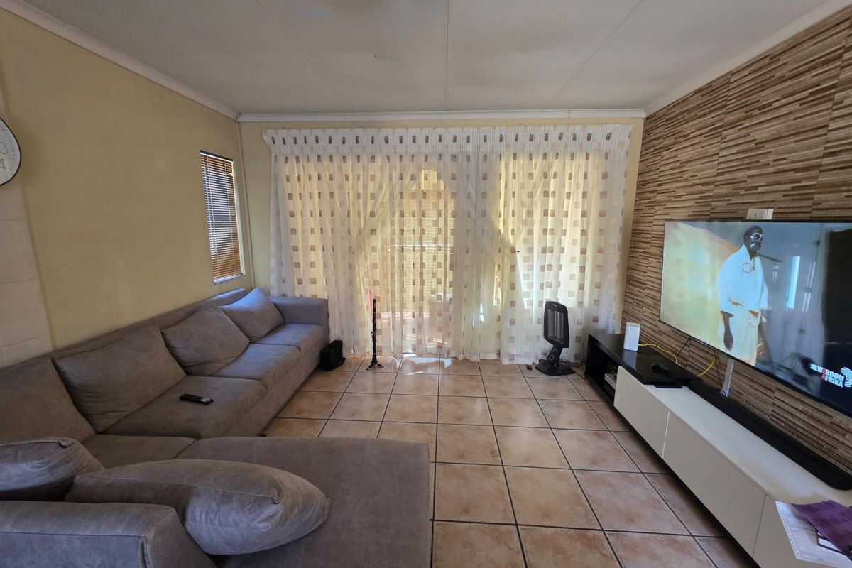 A living room featuring ceramic floor tiles, a textured feature wall, and a sliding glass door with curtains leading to an outdoor area.