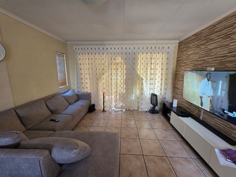A living room featuring ceramic floor tiles, a textured feature wall, and a sliding glass door with curtains leading to an outdoor area.