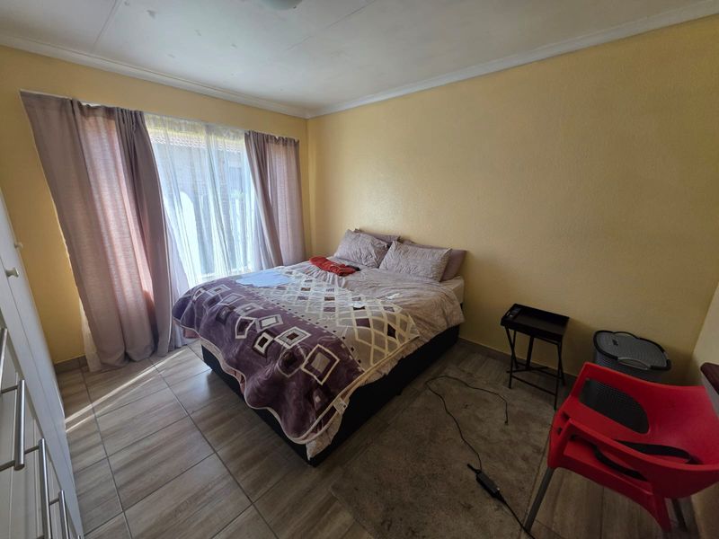 A functional bedroom featuring tiled flooring, a built-in wardrobe, and a sliding glass door providing natural light.